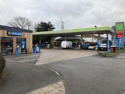 Petrol station with a Greggs on the left and a sign across the top saying 'Low Fuel Prices Always'.