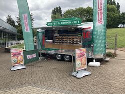 A van with a sign saying coffee & doughnuts, and Krispy Kreme flags.