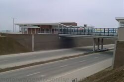 An open-air bridge with picnic tables, above a motorway.