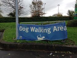 A sign saying dog walking area on a small grass patch.