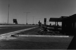 Black and white photo of the edge of a Heron-branded forecourt next to a dual carriageway.
